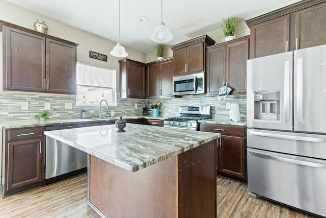 kitchen with appliances with stainless steel finishes, a center island, light stone counters, and decorative light fixtures