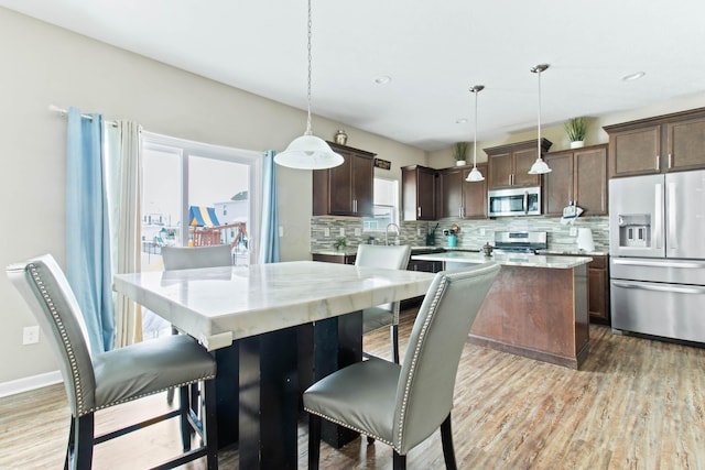 kitchen featuring hardwood / wood-style floors, pendant lighting, backsplash, a center island, and stainless steel appliances