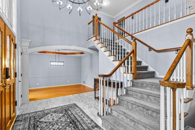 stairs featuring crown molding, wood-type flooring, a chandelier, and a high ceiling