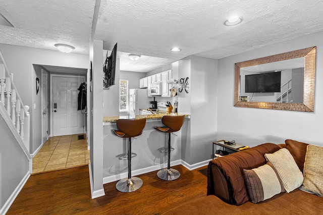 kitchen with white appliances, white cabinetry, dark hardwood / wood-style floors, a kitchen bar, and kitchen peninsula