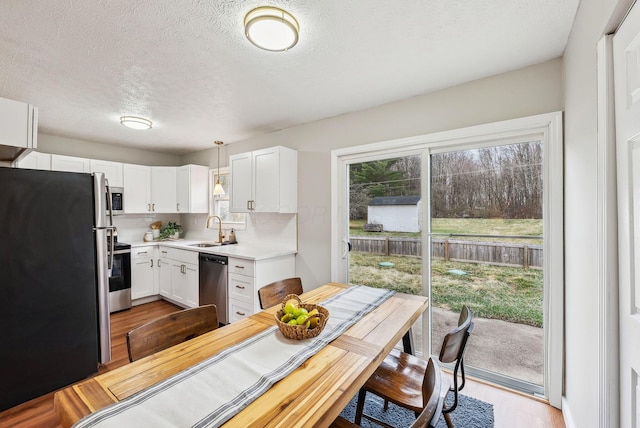 kitchen with sink, pendant lighting, stainless steel appliances, light hardwood / wood-style floors, and white cabinets