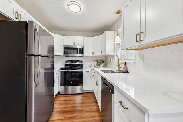 kitchen with pendant lighting, sink, appliances with stainless steel finishes, light stone counters, and white cabinets