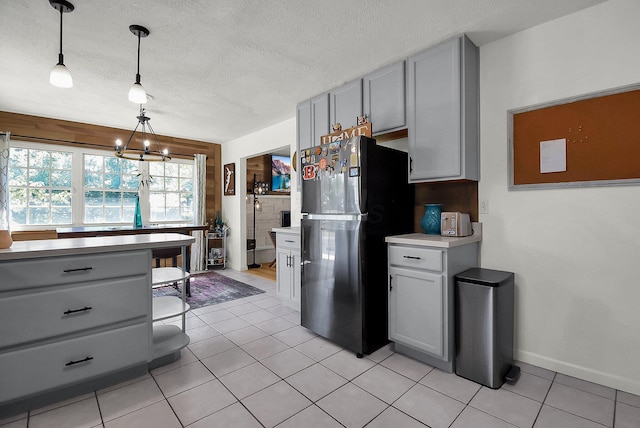 kitchen with black refrigerator, hanging light fixtures, light tile patterned floors, and gray cabinets