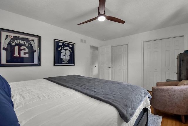 bedroom featuring hardwood / wood-style floors, a textured ceiling, multiple closets, and ceiling fan