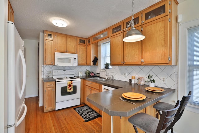 kitchen with sink, a breakfast bar area, kitchen peninsula, pendant lighting, and white appliances