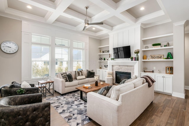 living room with ceiling fan, a stone fireplace, coffered ceiling, dark wood-style floors, and beamed ceiling