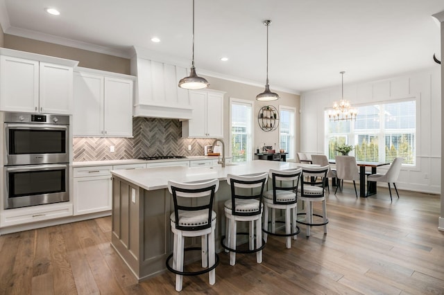 kitchen featuring double oven, light countertops, decorative light fixtures, and an island with sink