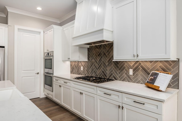 kitchen featuring appliances with stainless steel finishes, premium range hood, white cabinetry, and light stone countertops