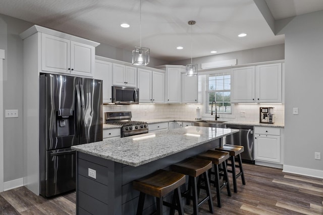 kitchen with sink, appliances with stainless steel finishes, a kitchen island, pendant lighting, and white cabinets