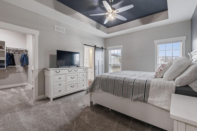 bedroom with a spacious closet, light carpet, a tray ceiling, ceiling fan, and a barn door