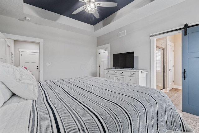 bedroom featuring ceiling fan, a tray ceiling, and a barn door