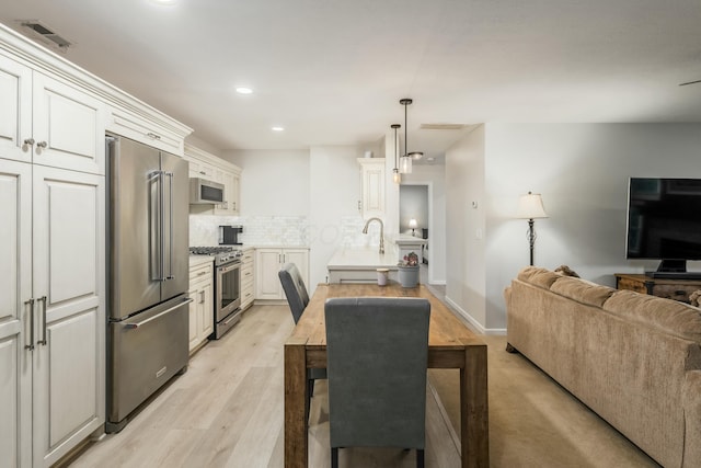 kitchen with light hardwood / wood-style flooring, white cabinetry, tasteful backsplash, premium appliances, and decorative light fixtures