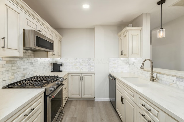 kitchen featuring appliances with stainless steel finishes, decorative light fixtures, tasteful backsplash, sink, and light hardwood / wood-style flooring