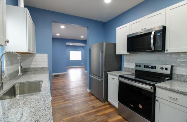 kitchen with sink, dark wood-type flooring, appliances with stainless steel finishes, white cabinetry, and light stone counters