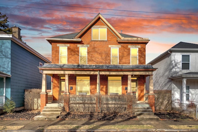 view of front of property with covered porch, brick siding, and fence