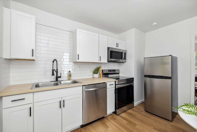 kitchen featuring sink, white cabinets, decorative backsplash, stainless steel appliances, and light hardwood / wood-style flooring