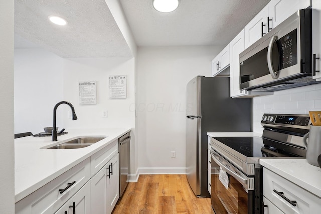 kitchen featuring stainless steel appliances, light hardwood / wood-style floors, sink, tasteful backsplash, and white cabinets