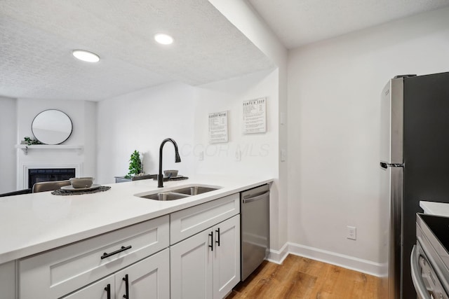 kitchen with appliances with stainless steel finishes, sink, light wood-type flooring, a textured ceiling, and white cabinets