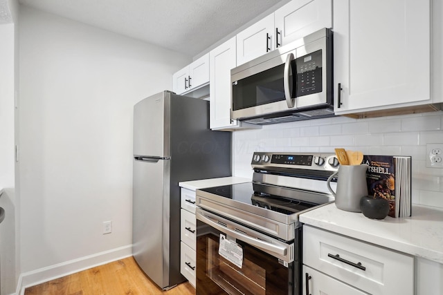 kitchen featuring light wood-type flooring, stainless steel appliances, white cabinets, and backsplash