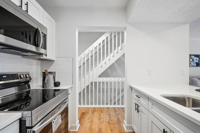 kitchen featuring appliances with stainless steel finishes, a textured ceiling, decorative backsplash, light hardwood / wood-style floors, and white cabinetry