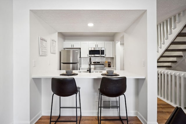 kitchen featuring radiator heating unit, appliances with stainless steel finishes, white cabinetry, and a breakfast bar area