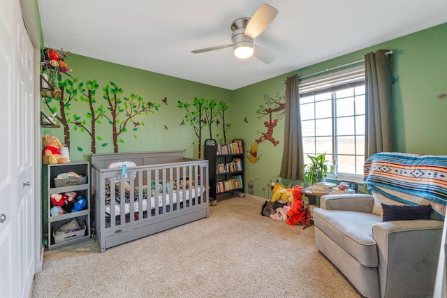 carpeted bedroom with a nursery area, ceiling fan, and baseboards