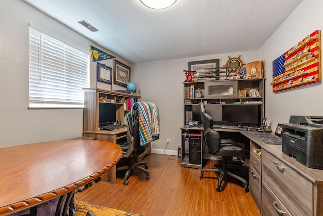 office with a textured ceiling, wood finished floors, visible vents, and baseboards