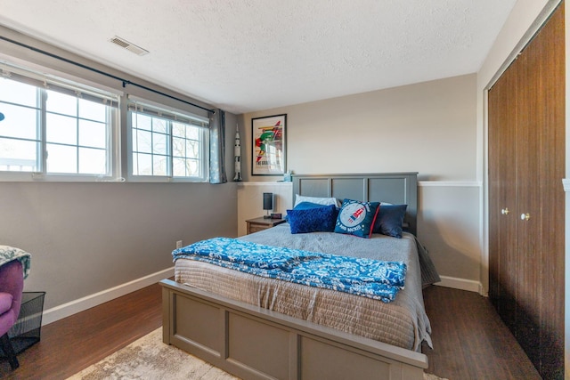 bedroom featuring baseboards, a textured ceiling, visible vents, and wood finished floors