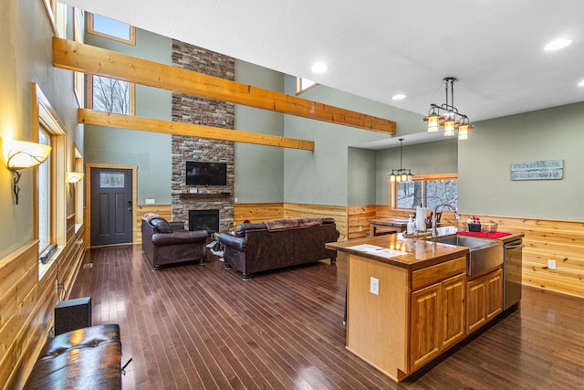 kitchen with a fireplace, sink, hanging light fixtures, stainless steel dishwasher, and a center island with sink