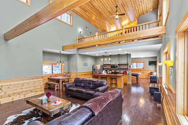 living room with wood ceiling, dark wood-type flooring, beam ceiling, ceiling fan with notable chandelier, and wood walls