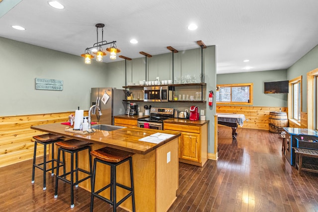 kitchen featuring butcher block countertops, sink, stainless steel appliances, a kitchen breakfast bar, and decorative light fixtures