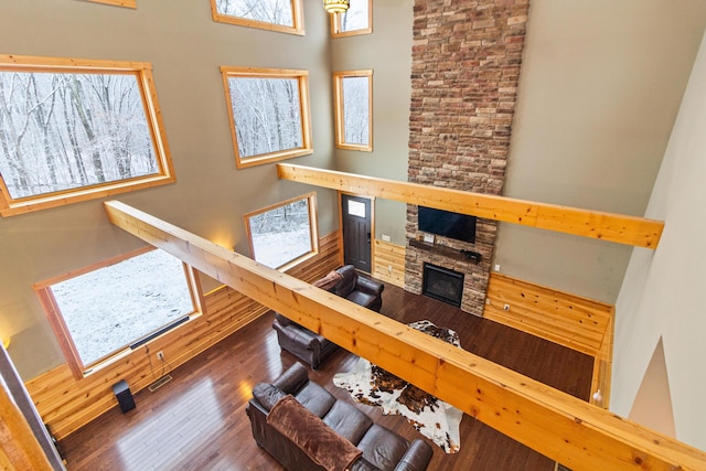 living room featuring a stone fireplace, wood-type flooring, and a towering ceiling