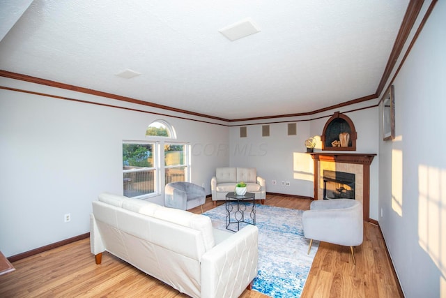 living room with ornamental molding, a tiled fireplace, light hardwood / wood-style flooring, and a textured ceiling