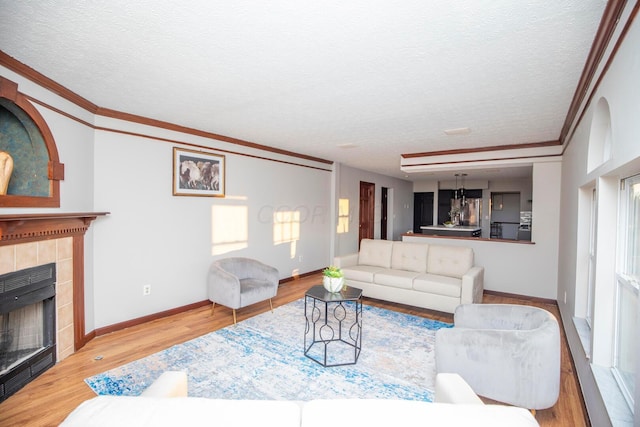 living room with ornamental molding, a textured ceiling, a tile fireplace, and light wood-type flooring