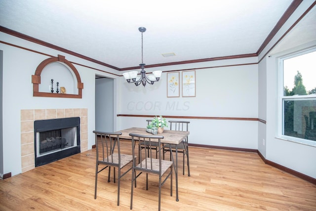 dining area featuring a tiled fireplace, light hardwood / wood-style flooring, ornamental molding, and a chandelier