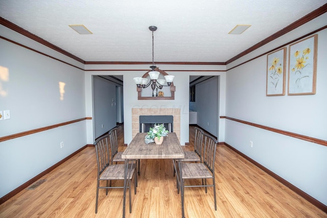 dining space with a tiled fireplace, ornamental molding, a chandelier, and light hardwood / wood-style floors