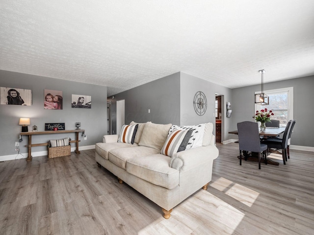 living room with light wood-style floors, a textured ceiling, and baseboards