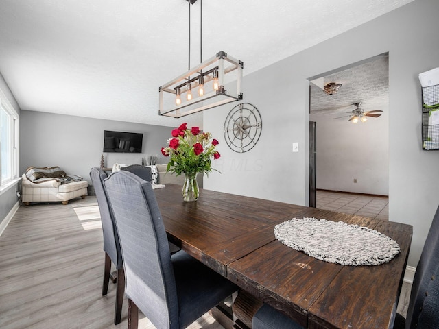 dining room with light wood-style floors, a ceiling fan, baseboards, and a textured ceiling