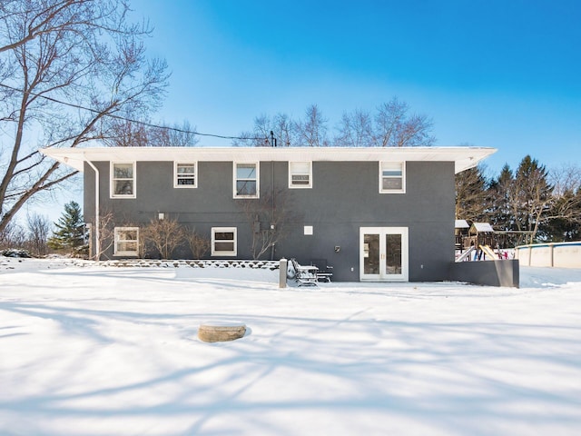 snow covered rear of property with french doors and stucco siding