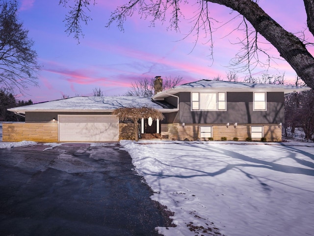 split level home featuring an attached garage, a chimney, and aphalt driveway