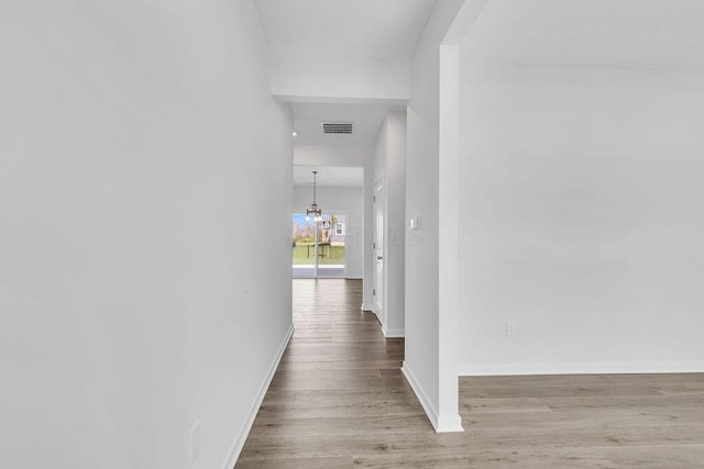 hallway featuring an inviting chandelier, wood finished floors, visible vents, and baseboards
