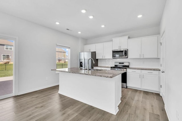 kitchen with white cabinets, stainless steel appliances, a kitchen island with sink, a sink, and visible vents