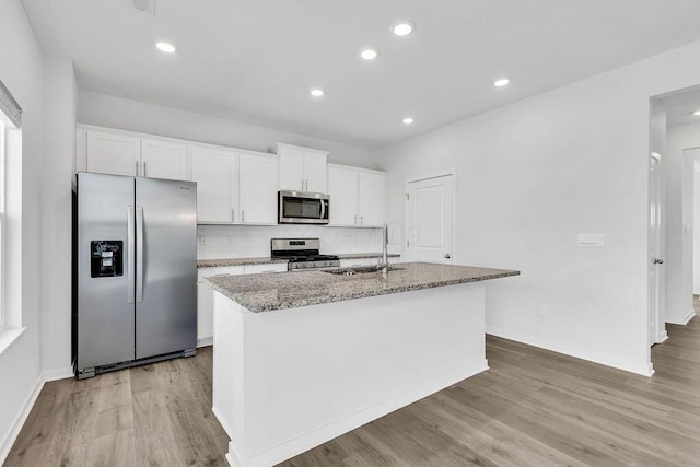 kitchen featuring light wood finished floors, stainless steel appliances, a kitchen island with sink, a sink, and white cabinetry