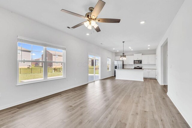 unfurnished living room with baseboards, recessed lighting, ceiling fan with notable chandelier, and light wood-type flooring