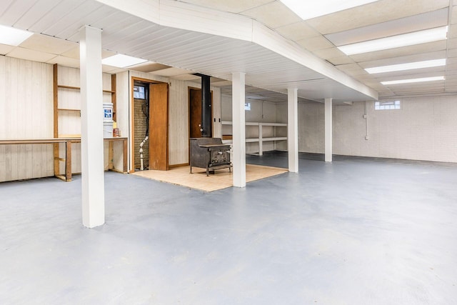 below grade area with a paneled ceiling, brick wall, and a wood stove