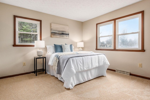 bedroom featuring light carpet, visible vents, a textured ceiling, and baseboards