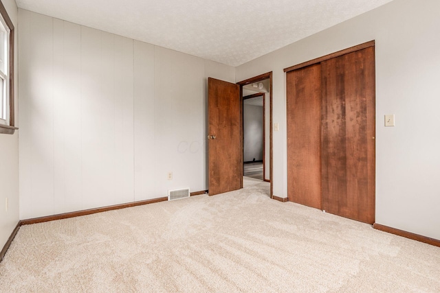 unfurnished bedroom featuring baseboards, visible vents, a closet, a textured ceiling, and carpet flooring