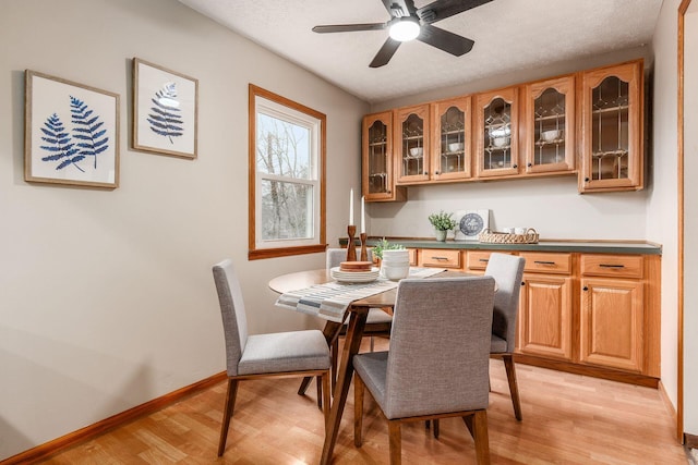 dining room featuring ceiling fan, baseboards, a textured ceiling, and light wood-style flooring