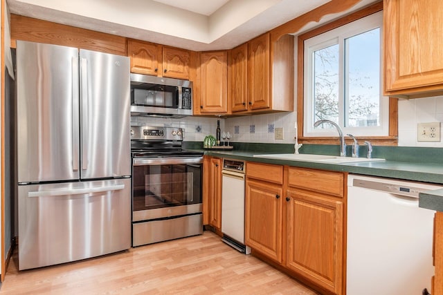 kitchen with light wood finished floors, dark countertops, decorative backsplash, stainless steel appliances, and a sink