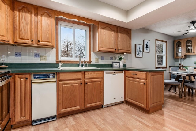 kitchen featuring brown cabinets, a sink, dark countertops, light wood-style floors, and dishwasher